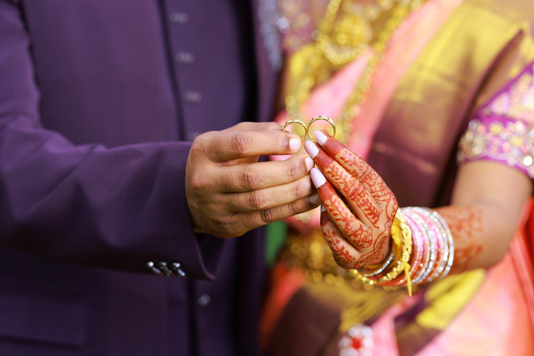 Two gold engagement rings held between Teja and Lekha's fingers